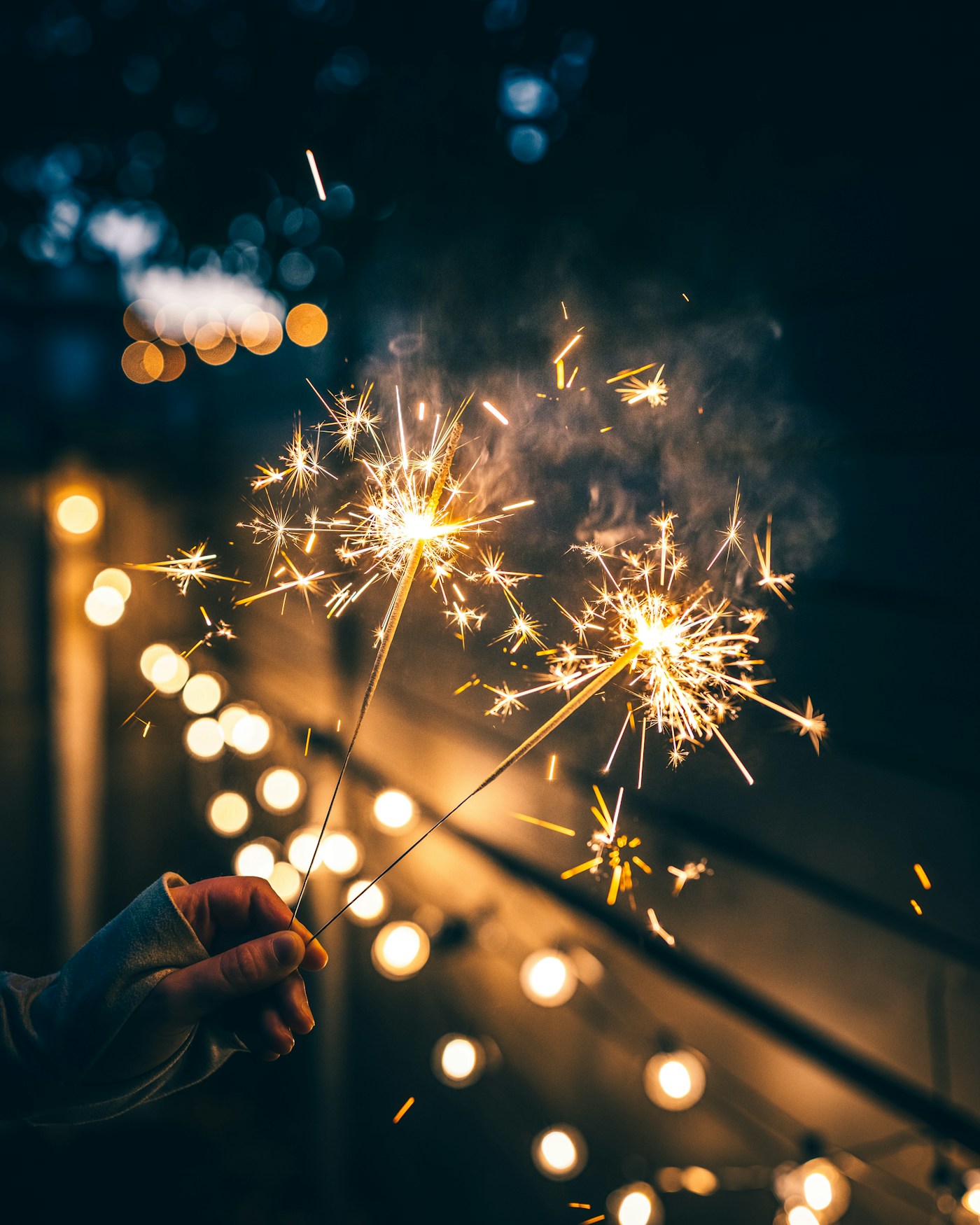 A hand holding a sparkler against warm evening lights